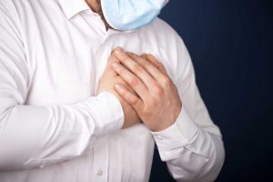 Man wearing medical face mask with chest pain - heart attack, shortness of breath during work in office.